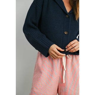 Person wearing a navy cardigan and red striped pants against a gray background