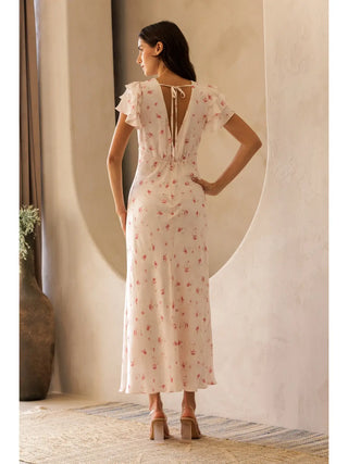 Woman wearing a floral dress standing in a room with neutral decor.