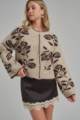 Woman wearing a patterned cardigan over a black skirt with lace hem on a gray background
