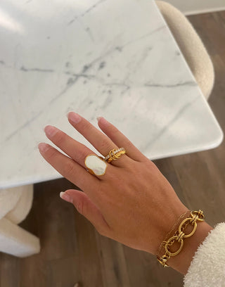 Hand wearing a gold ring and bracelet on a marble surface