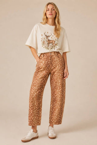 Woman wearing a white t-shirt with a deer graphic and patterned pants on a beige background