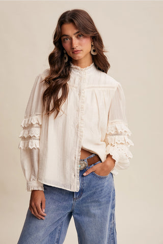 Woman wearing a white blouse with ruffled sleeves and blue jeans on a beige background