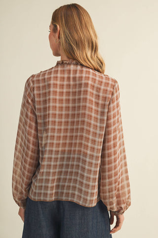 A woman shown from the back wearing a long-sleeve plaid button-up shirt in rust brown, beige, and white, paired with dark blue jeans, against a plain light beige background.