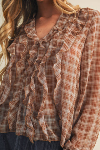 A close-up of a woman wearing a long-sleeve ruffled blouse with a brown, beige, and white plaid pattern.