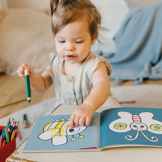 Child playing with a coloring book and crayons on a table.
