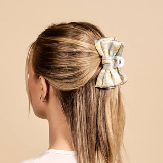 Person with blonde hair tied with a decorative bow hair clip on a beige background
