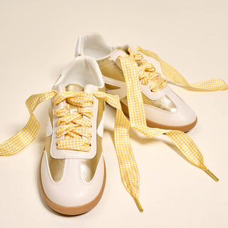 White sneakers with yellow gingham shoelaces on a beige background