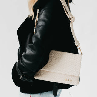 Beige handbag with braided handle worn over a black leather jacket on a light background