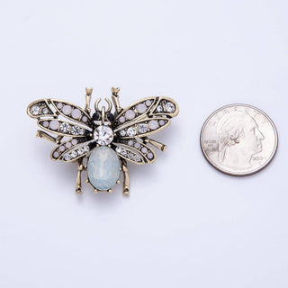 Butterfly-shaped brooch with gemstone next to a quarter for scale on a light purple background