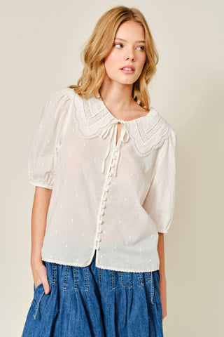Woman wearing a white blouse with lace details and blue jeans on a plain background