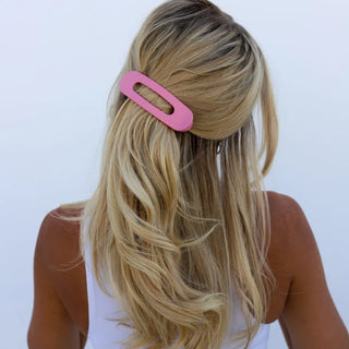 Person with long blonde hair wearing a pink hair clip on a white background