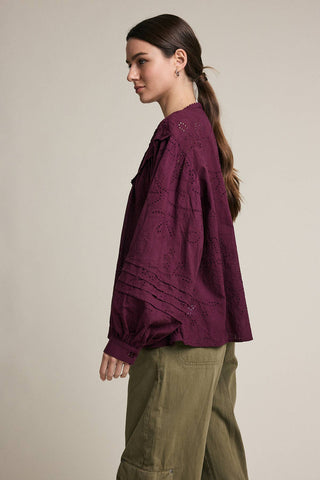 Woman wearing a purple shirt and green pants against a beige background