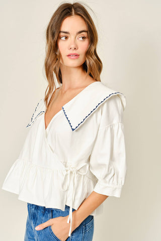 Woman wearing a white blouse with blue trim on a beige background