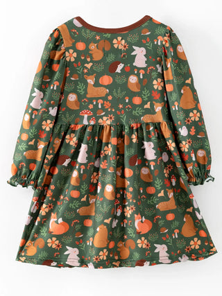 A long-sleeve children's dress with a dark green autumn-themed print featuring pumpkins, squirrels, rabbits, and flowers, shown against a plain white background.