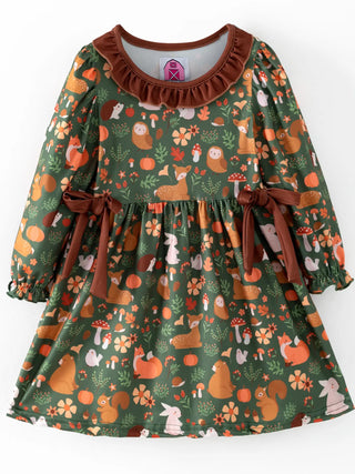 A toddler girl's long-sleeve dress with a forest-themed print featuring squirrels, rabbits, mushrooms, and pumpkins on a dark green background, finished with a brown ruffled collar and matching brown ribbon ties at the waist.
