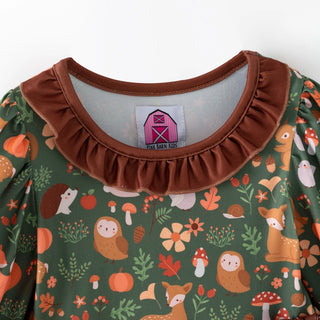 Close-up of a children's long-sleeve top by Love Barn Kids, featuring a green base with an autumn woodland print of owls, foxes, pumpkins, and mushrooms, finished with a brown ruffled collar.