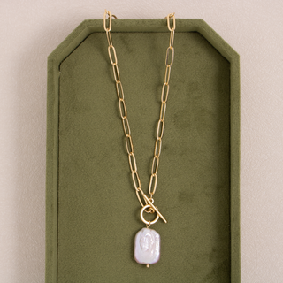 Gold chain necklace with a pendant on a green stand