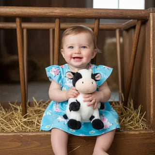 baby wearing blue romper with barn background holding cow