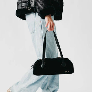 Person holding a black handbag with a plain background