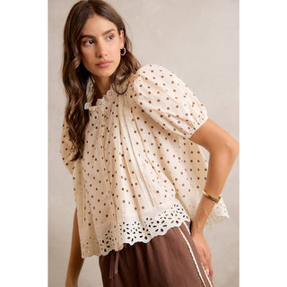 Woman wearing a beige blouse with brown polka dots and brown pants against a neutral background
