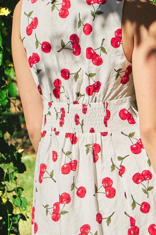 White dress with red cherry pattern worn by a person outdoors.