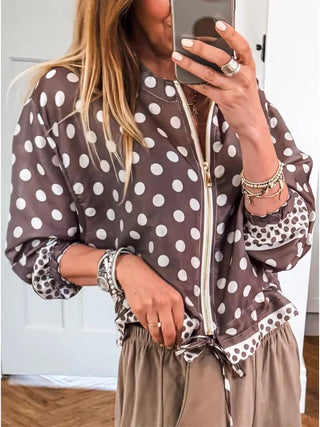 A woman takes a mirror selfie wearing a brown and white polka dot zip-up jacket with leopard-print trim and beige drawstring pants.