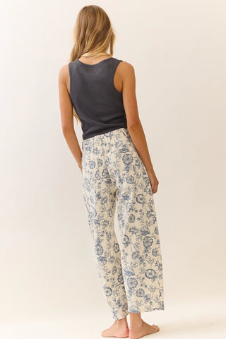 Woman wearing a sleeveless top and floral pants on a plain background