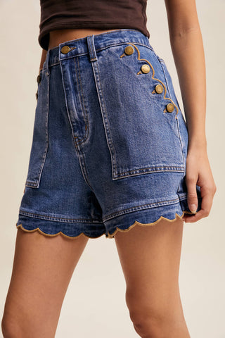 Denim shorts with scalloped hem and decorative buttons on a neutral background