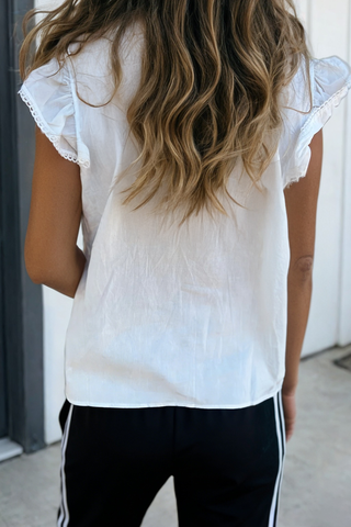 Person wearing a white blouse with ruffled sleeves and black pants with white stripes.