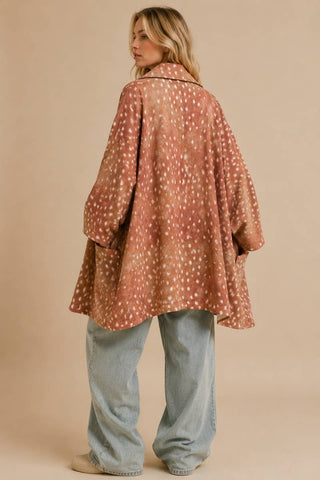 A woman shown from the back wearing a dusty rose-brown open-front cardigan with a white dalmatian spot pattern, paired with light-wash wide-leg jeans, against a solid beige studio background.