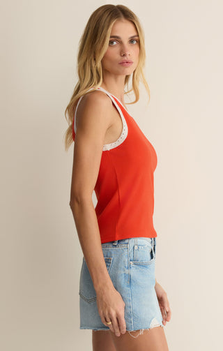Woman wearing a red tank top with lace trim and denim shorts on a beige background