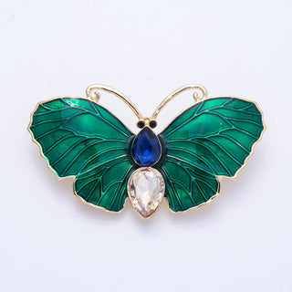 Butterfly-shaped brooch with green wings, blue and clear gemstones on a white background