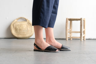 Person wearing black sandals standing on a light wooden floor with a neutral background