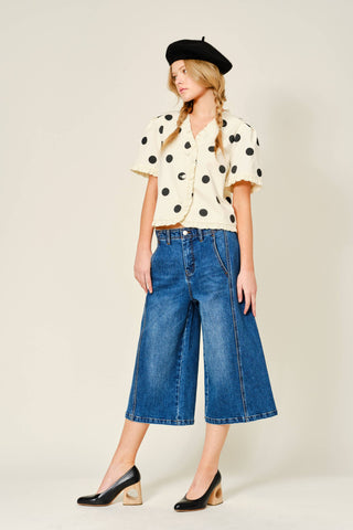 Woman wearing a polka dot blouse, blue jeans, and a black beret on a white background