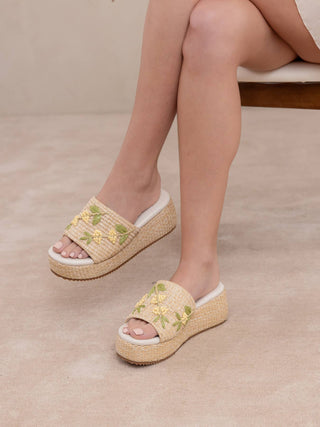 Person wearing beige sandals with floral embroidery on a neutral background
