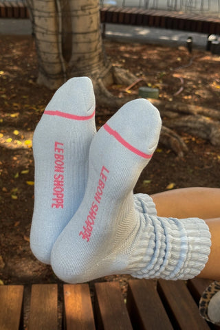 Gray socks with pink accents and 'Lebon Shoppe' branding on a wooden bench.
