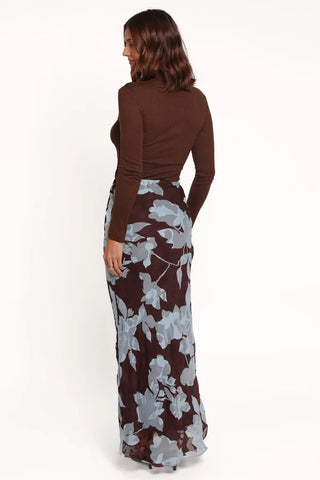A woman shown from the back wearing a brown long-sleeve mock-neck top and a dark brown maxi skirt with a light gray floral pattern, against a plain white background.