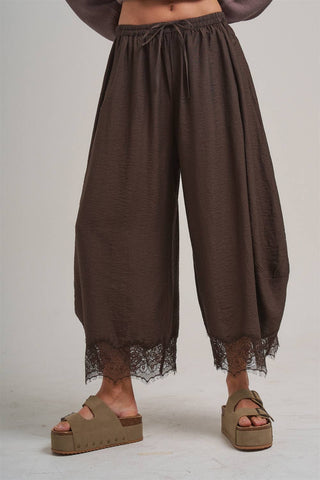 Brown wide-leg pants with lace trim worn by a person on a plain background