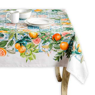 A rectangular tablecloth with a Mediterranean tile pattern and orange motifs, styled on a table with white plates and a white mug, set against a clean white background.