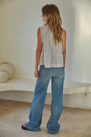 Woman wearing a sleeveless top and blue jeans standing in a minimalistic room.