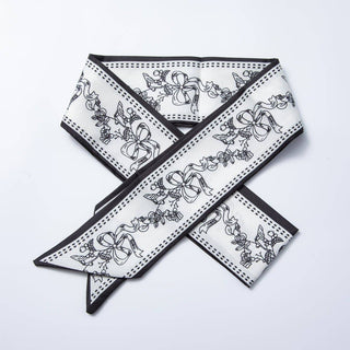 White scarf with black floral and bow pattern on a light gray background