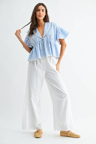 Woman wearing a blue checkered top and white pants on a white background