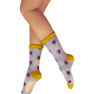 Gray socks with ladybugs and yellow accents worn by a person on a white background