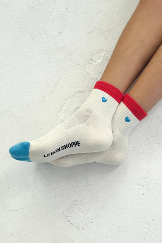 White socks with red cuffs and blue toes worn by a person on a light gray background