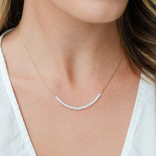 Gold necklace with small beads worn by a person against a neutral background