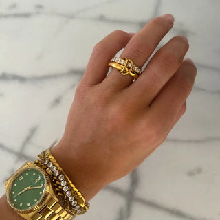 Hand wearing a gold watch and ring on a marble surface