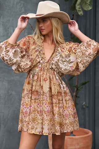 Woman wearing a floral dress and cowboy hat against a gray wall.