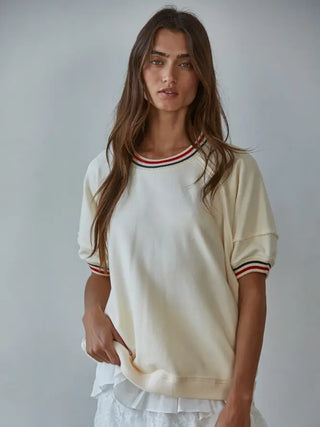 Woman wearing a cream-colored sweater with red and black stripes on a plain background