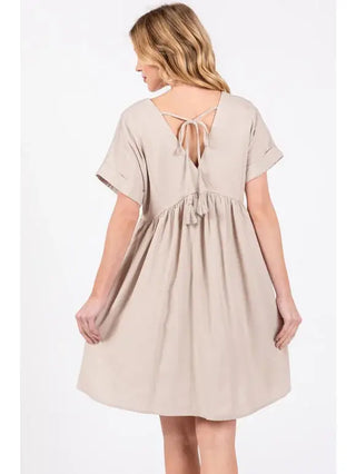 Woman wearing a beige dress with a tie-back detail on a white background