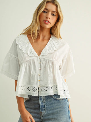 Woman wearing a white blouse with lace details and blue jeans on a plain background